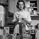1960s WOMAN HOUSEWIFE IN KITCHEN CHECKING GROCERY FOOD