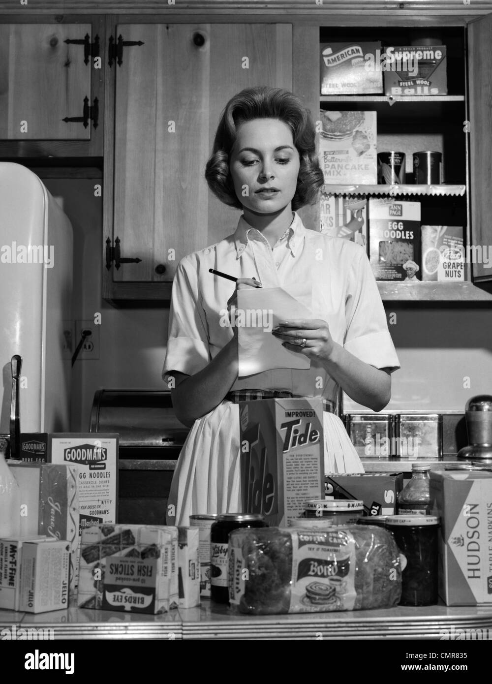1960s WOMAN HOUSEWIFE IN KITCHEN CHECKING GROCERY FOOD 
